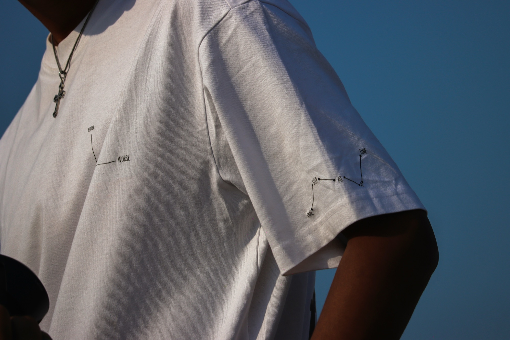 Biały t-shirt z nadrukiem One Step At A Time na tle nieba